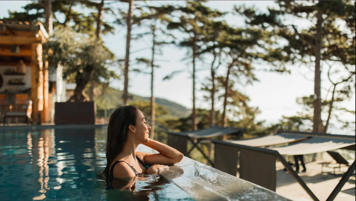 A woman relaxing in an outdoor infinity pool surrounded by trees and mountain views, enjoying a peaceful moment.
